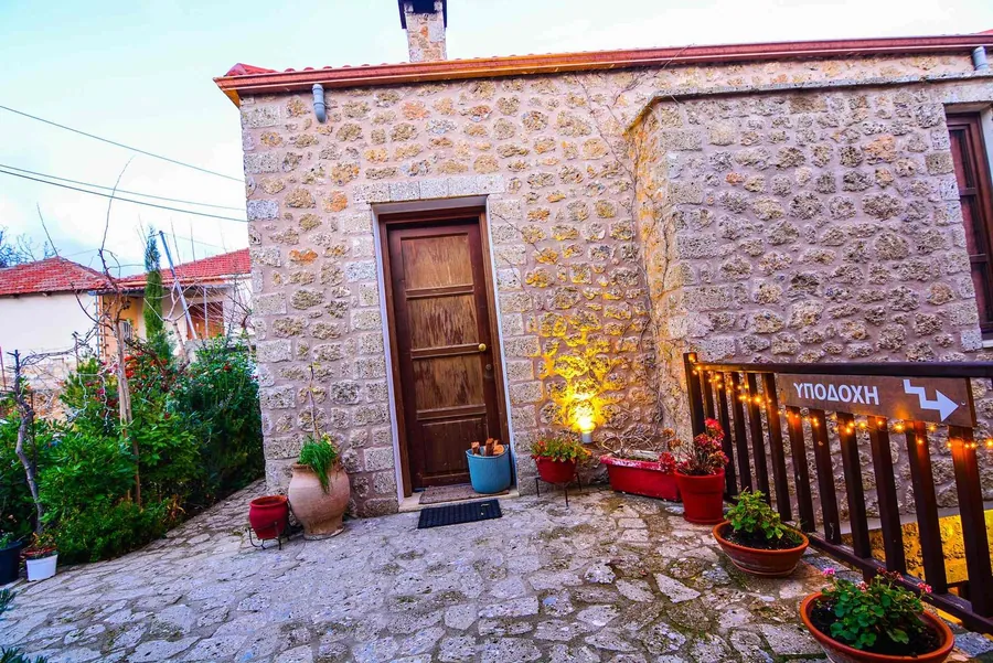 Η πέτρινη είσοδος με την ξύλινη πόρτα, γλάστρες και φωτάκια